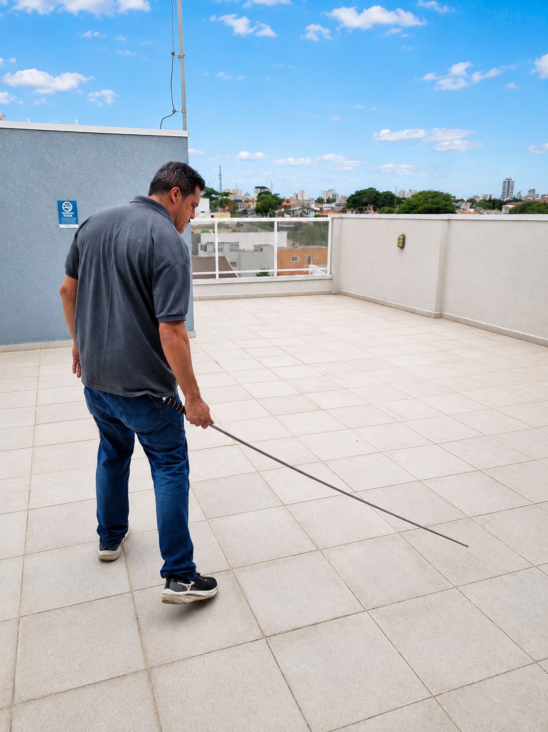 Engenheiro Vallero checando a cobertura de um prédio durante inspeção predial, avaliando revestimentos de piso cerâmico com haste telescópica e teste de percussão.
